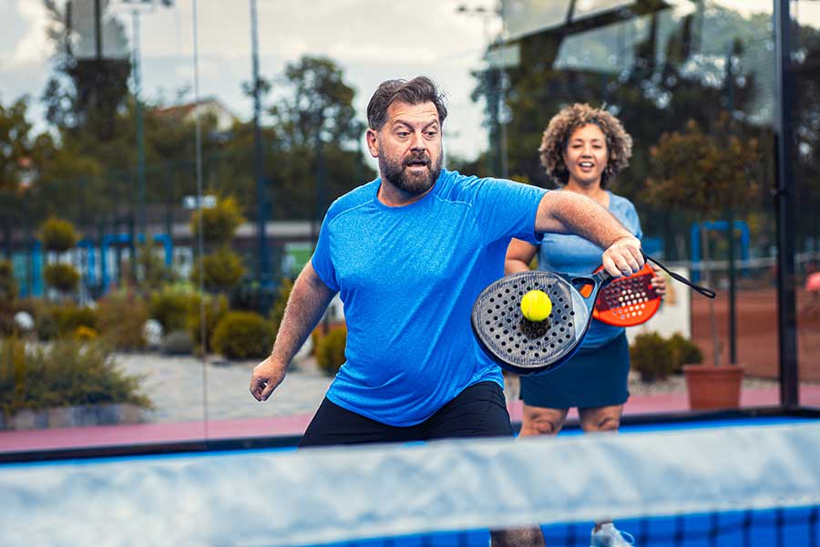 Mixed adult couple palying padel on outdoor court.